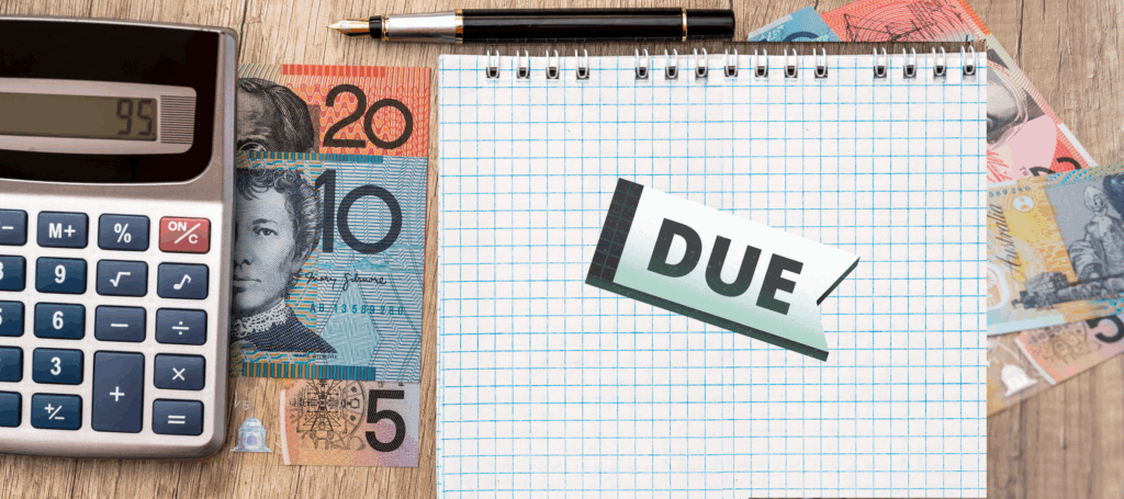 Stacks of Australian dollars are strewn across a desk along with a calculator, pen, and a notebook with a tag that says "Due" on it.