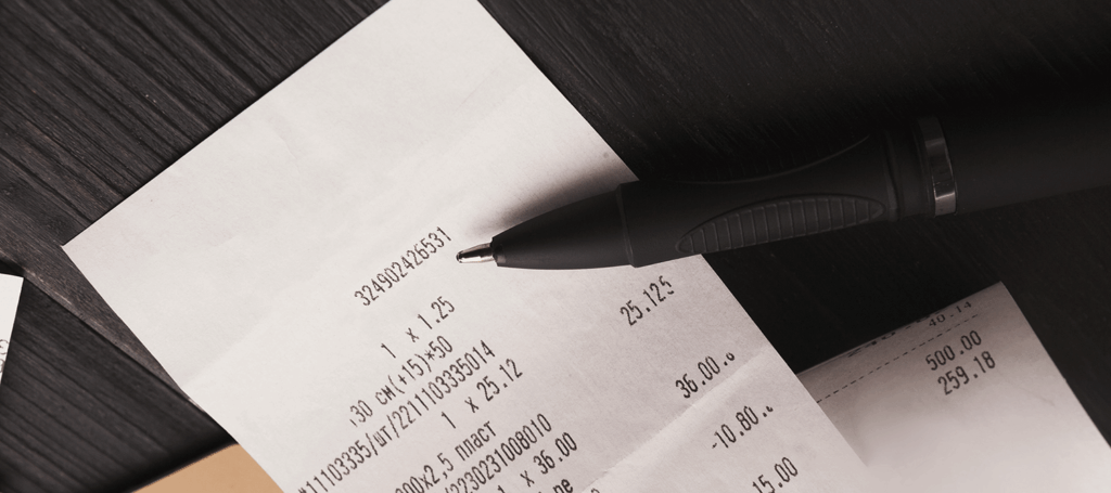 A white receipt sits against a black desk. More receipts and a pen also lay on the desk.
