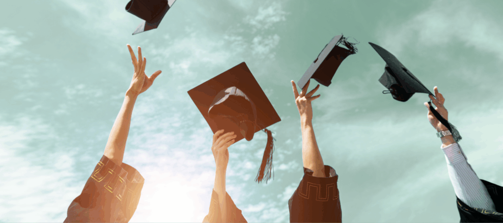 Four arms are seen throwing their graduation caps into the air amidst a blue-green sky with wispy clouds in the background.